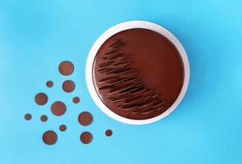 Dark chocolate mousse cake covered with mirror glaze and decorated with round chocolate chips on blue background. Modern stylish cake. Flat lay style. Copy space.