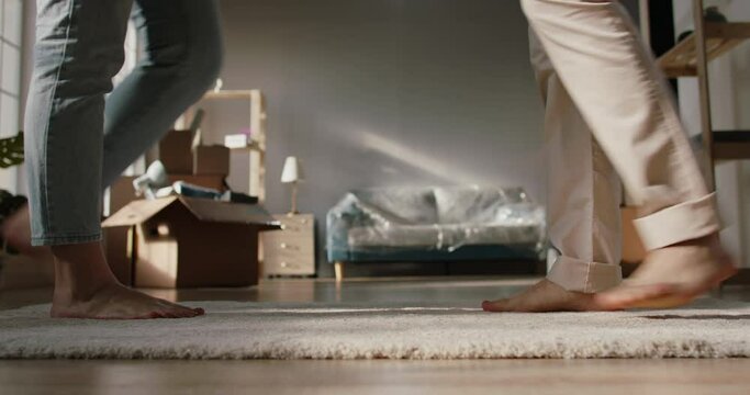 Close-up low angle shot of legs of a cute couple walking barefoot on floor of their new home. Girl standing on tip-toes to kiss her boyfriend - love, new life concept 4k footage