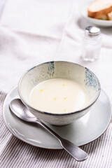 Cauliflower and Potato Cream Soup served with herbs and pepper on white linen striped tablecloth. Selective focus