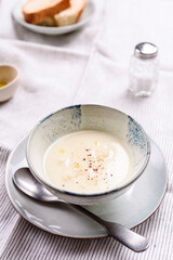 Cauliflower and Potato Cream Soup served with herbs and pepper on white linen striped tablecloth. Selective focus