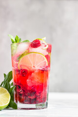 Lemonade or non-alcohol cocktail with raspberry, lime and mint in glass on grey stone background. Summer berry drink.