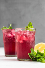 Sparkling pink lemonade with lemon and mint on light grey concrete background. Summer refreshment drink.