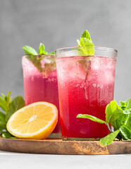 Cold sparkling hibiscus or karkade tea with lemon, mint and ice in glasses on a grey stone background. Summer drink, lemonade.