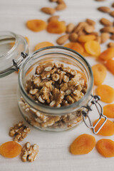 Raw walnut in a glass jar, dried apricot and almond nuts on wooden table