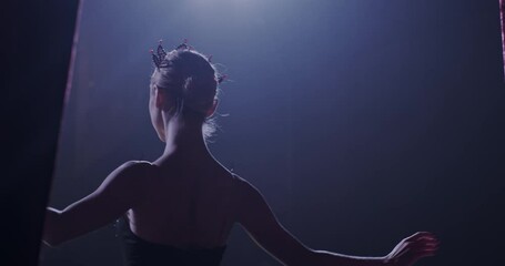 Rear on Caucasian graceful and famous ballerina in black dress and crown coming out on stage from curtains and bowing. Back view on female ballet dancer entering the stage to bow.