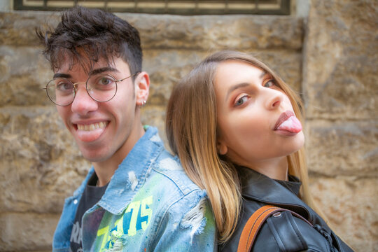 Un giovane uomo e una bellissima donna italiana mostrano la lingua in una posa molto divertente lui con giacca di jeans e occhiali da vista e le con giacca di pelle nera 