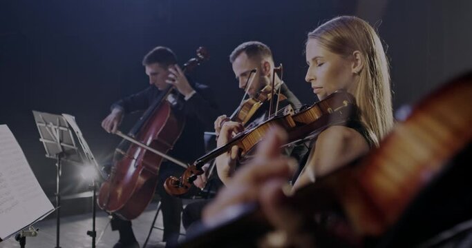 Classical entertainment concept. Male and female orchesta of classic music performing on stage of theater. Musicians playing on cello and violins at rehearse.