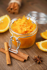 A jar of orange confiture with slices of orange fruit, cinnamon and star anise on the wooden background, homemade orange jam with the few pieces of bread on the wooden table