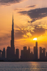 Obraz premium Dubai skyline at sunset during golden hour, sun setting over Dubai skyline; silhouette of Dubai skyline