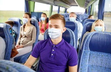 transport, tourism, road trip and people concept - young man wearing face protective medical mask for protection from virus disease sitting in travel bus or train