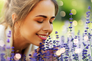gardening and people concept - close up of happy young woman smelling lavender flowers at summer garden over festive lights background