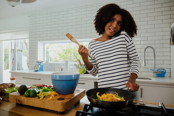 Mixed race woman talking on a smartphone while cooking in the kitchen