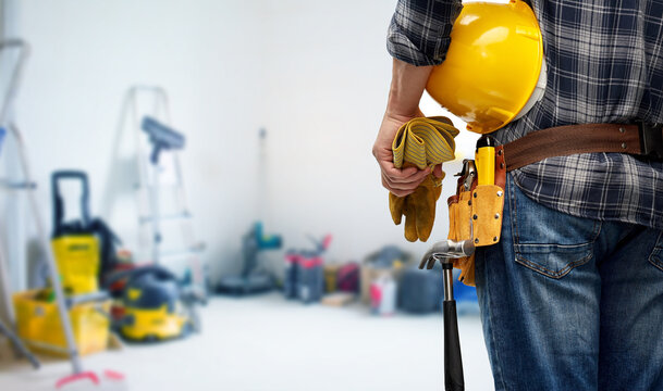 repair, construction and building - male worker or builder with helmet and working tools on belt over utility room background