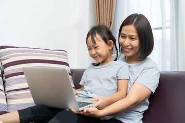 Asian mother and daughter using laptop studying homework online lesson at home, Social distance online education idea concept