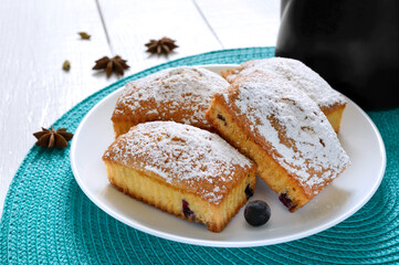 Cupcakes with berries and icing sugar on a plate on a white wooden background. Rectangular muffins and tea