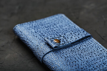 Blue purse made of textured leather on a black background.
