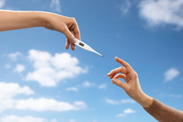 hygiene, health care and safety concept - close up of male hand giving thermometer to woman over blue sky and clouds background