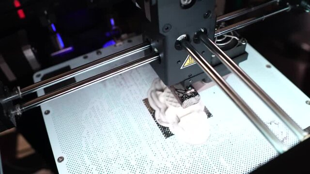 A sculpture is maufactered by a 3D-printer from plastic in a dark stylish surrounding