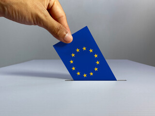 Voting / election concept: hand holding voting card with country national flag, inserting it into...