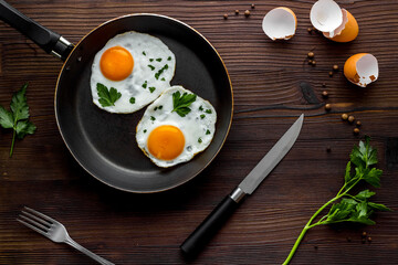 Fried eggs on frying pan on wooden table top-down