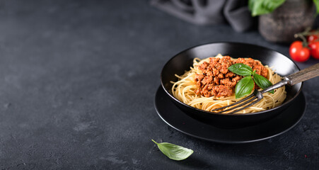 Italian pasta. Spaghetti bolognese in a black plate on a dark background. Place for text