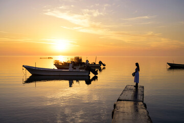 Silhouette woman standing on the pier with boats floating on sea water over colorful sunrise sky clouds background, Bahrain.
