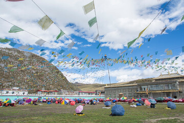 Many Tibetan monks praying outdoors under stretched Tibetan prayer flags.  Tagong, Kangding,...