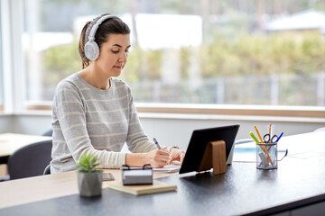 remote job, technology and people concept - young woman in headphones with tablet pc computer...