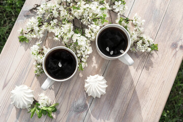 Two beautiful porcelain coffee cups with marshmallow dessert decorated with white cherry flowers on wooden table in spring garden in setting sun light. Flat lay style.