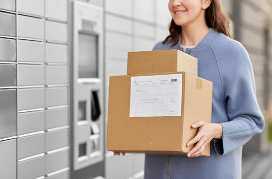 mail delivery and post service concept - close up of happy smiling woman with boxes at outdoor automated parcel machine