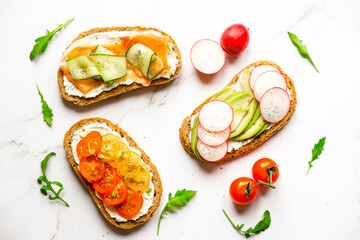 Top view variety of sandwiches for breakfast, snack, appetizers - avocado, radish, tomatoes, bacon, cucumbers, cream cheese, whole grain bread sandwiches. On a light background.