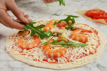 Woman adding arugula to pizza white marble table, closeup