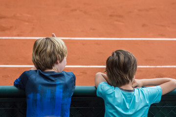 Two kids, facing backwards, watching a Tennis game in a clay court, during the French open...