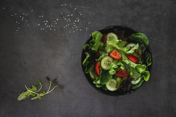 vegetable salad of fresh tomato, cucumber, cos, green and red oak lettuce ,sesame and sunflower sprouts on black bowl. Diet and vegetarian menu. concept for a tasty and healthy meal. top view.