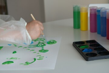 Boy painting with a brush and green paint a white paper