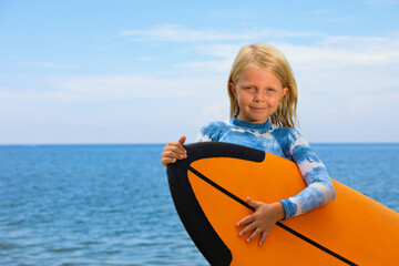 Happy baby girl - young surfer learn to ride on surfboard with fun on sea waves. Active family lifestyle, kids outdoor water sport lessons, swimming activity in surf camp. Summer vacation with child.