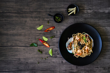 spicy spaghetti with shrimp, and mussel, on top with pepper on black plate. seafood pasta on a dish, chili, and corn on a wooden table. copy space.