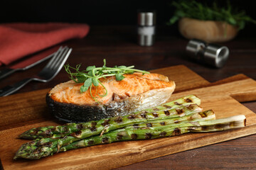 Tasty salmon steak served with asparagus and sprouts on wooden board