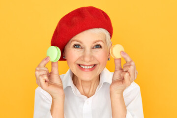 Isolated shot of adorable funny senior female pensioner in red bonnet smiling broadly at camera...