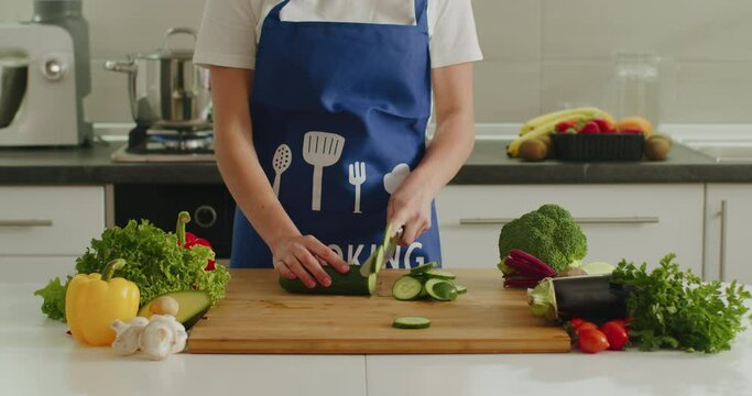 A woman is slicing cucumber on the kitchen board. Salad preparation. Water is boiling in the background. 4k