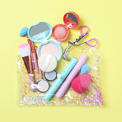 Naklejka premium Plastic cosmetic bag with makeup products and beauty accessories on yellow background, flat lay