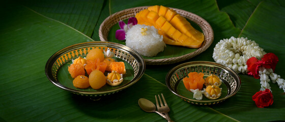 Cropped shot of several Thai traditional dessert serving on wooden tray and brass tray on banana leaves background