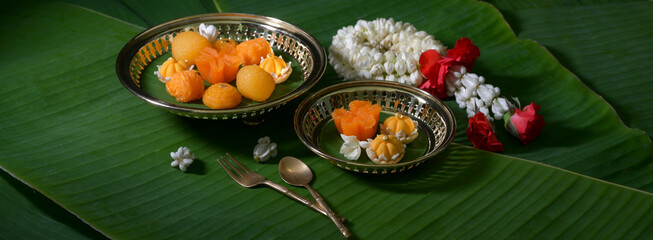 Several Thai traditional dessert serving on brass tray with brass cutlery and garland jasmine decorated on banana leaves