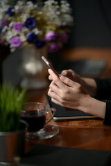 Fototapeta na wymiar Businesswoman using smartphone while sitting at wooden counter bar in coffee shop