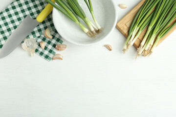 Flat lay composition with fresh green spring onions and garlic cloves on white wooden table. Space for text