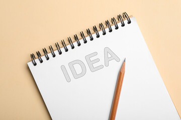 Notebook with word IDEA and pencil on beige background, top view