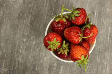 Strawberries ripe in a plate on a gray background, top view