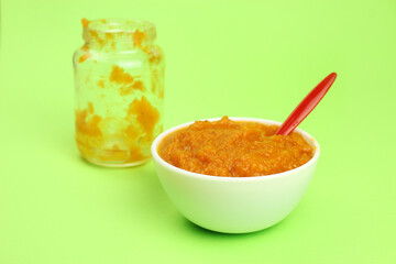 pumpkin porridge in a bowl with a spoon on a green background and an empty glass jar, baby or vegan food