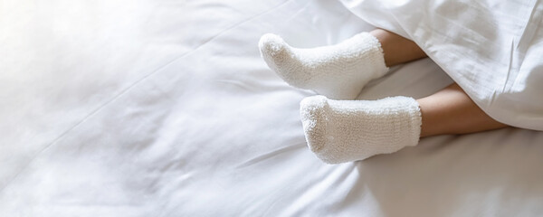 Woman feet in warm woolen socks on white bedclothes. Close up of young woman lying in bed at home....