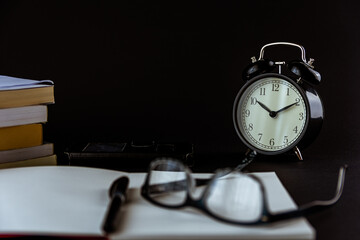Still life con reloj antiguo sobre escritorio con libros, reloj despertador, gafas y fondo negro o...